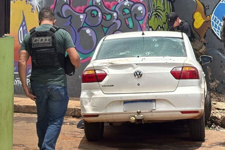 Carro perfurado por tiros em cena de crime no Jardim Nhanhá, Campo Grande, sob investigação policial.
