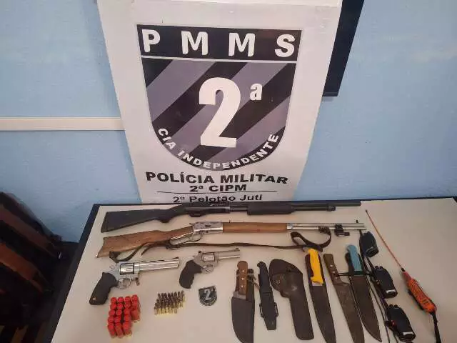 Caminhonete em estrada de terra com equipamentos de caça sobre o capô em cenário de fazenda
