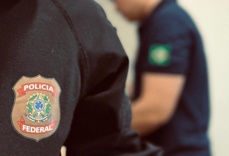 Distintivo da Polícia Federal com fronteira Brasil-Paraguai ao fundo.