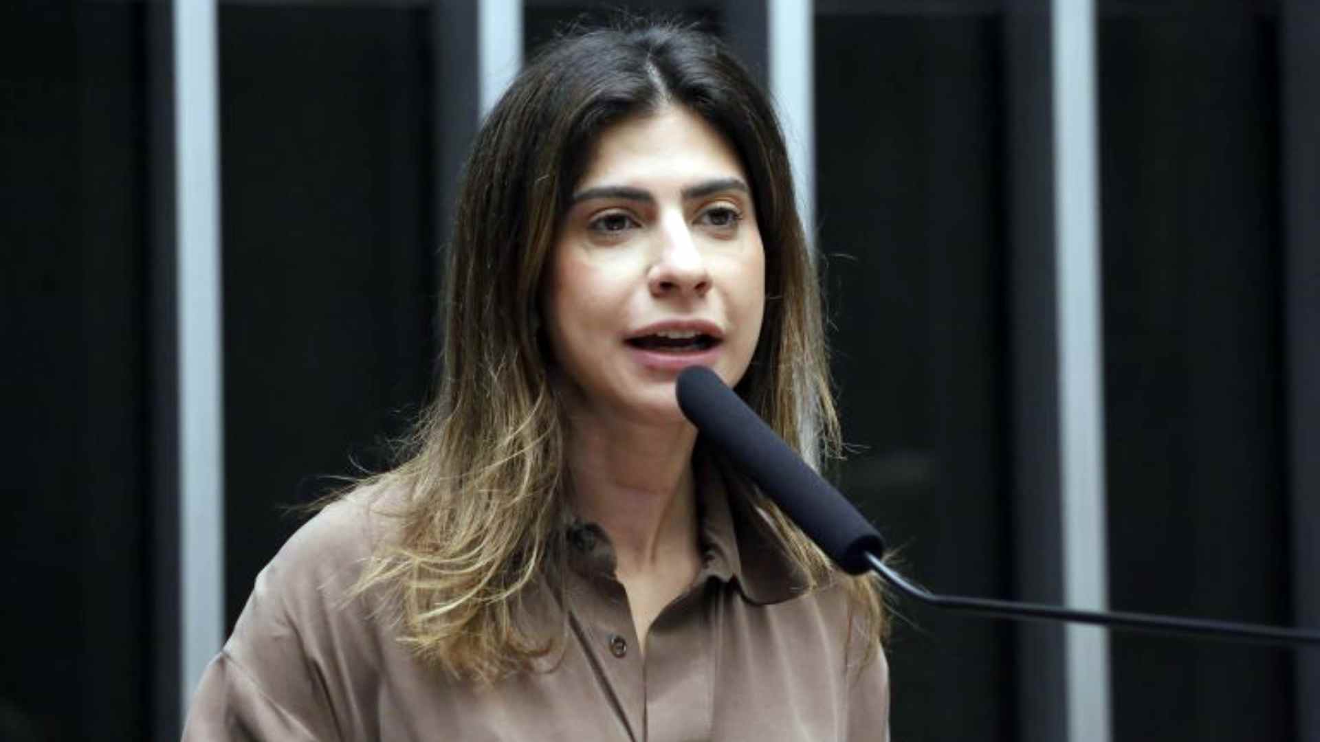 Camila Jara, deputada federal, falando em público, simbolizando a cobrança por transparência na Fiems.