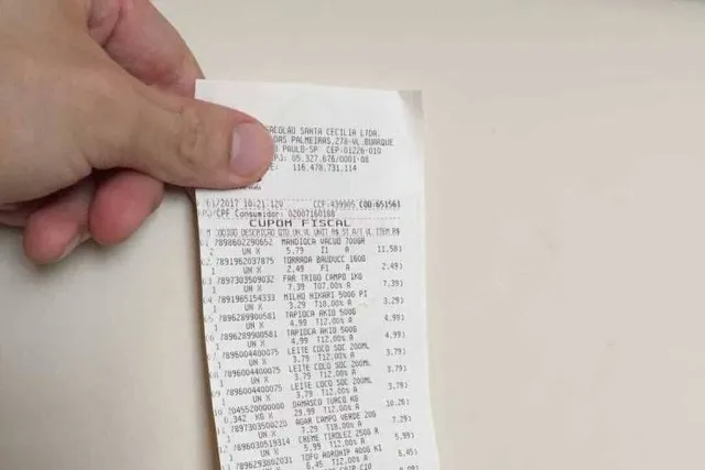 Ilustração de pessoa segurando celular com nota fiscal e CPF, moedas e confetes, representando o sorteio da Nota MS Premiada.