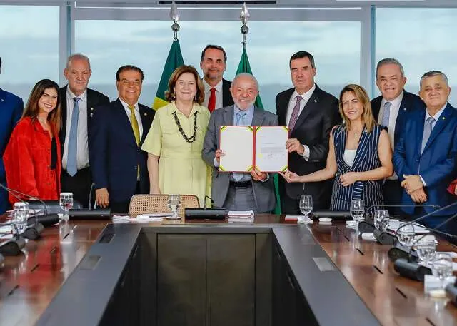 Presidente e governador assinando contrato no Palácio do Planalto durante cerimônia oficial com ministros ao fundo.