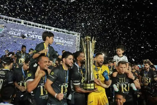 Jogadores do Operário erguem a taça de campeão sul-mato-grossense em meio à celebração no campo.