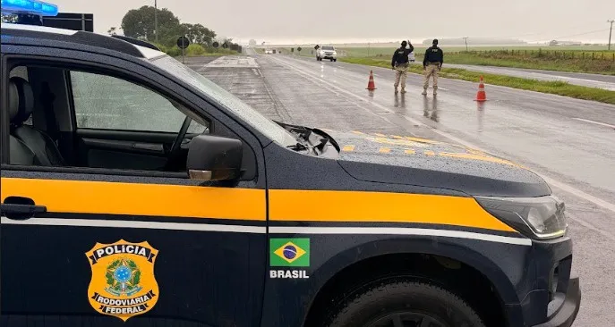 Agentes da PRF realizando fiscalização e teste de alcoolemia em rodovia federal de Mato Grosso do Sul, com viaturas e cones.