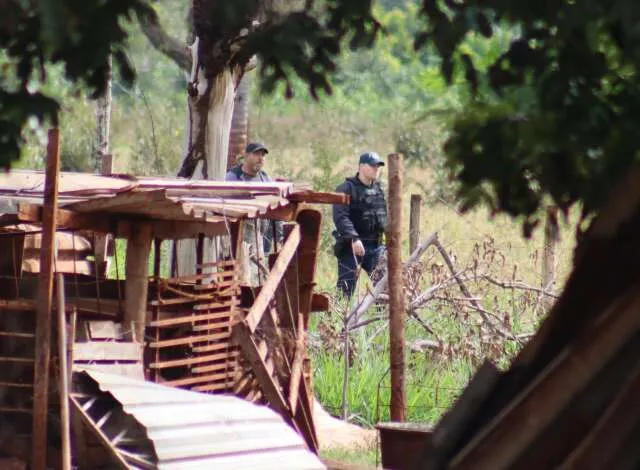 Chácara com fita de isolamento policial, viatura e investigadores em cena, sem vítimas.