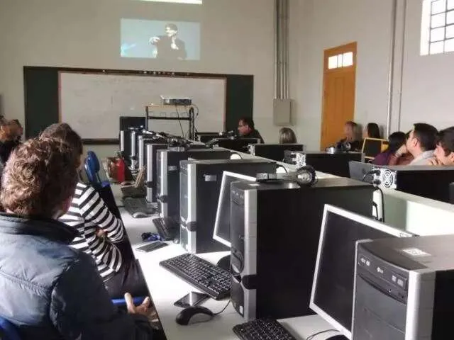 Sala de aula universitária com estudantes e professor em computadores, quadro com esquemas de pensamento computacional