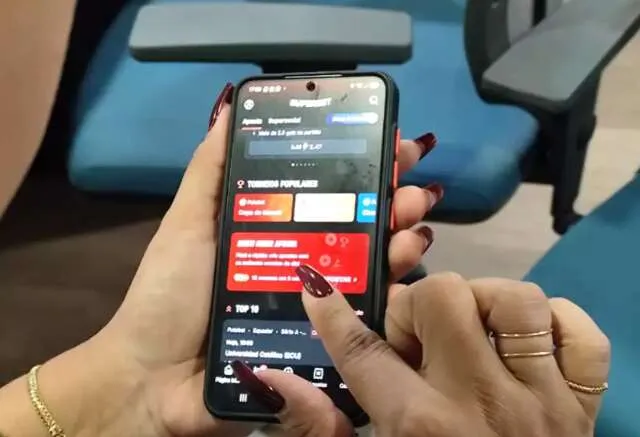 Pessoa preocupada em frente a laptop com site de apostas e documentos financeiros ao lado