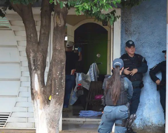Casa na Vila Bandeirantes isolada por fita de perícia, com viaturas policiais e ambulância ao fundo