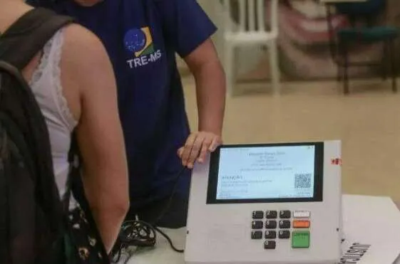Auditório com participantes e palco durante convenção partidária em Mato Grosso do Sul, com bandeiras e mesa principal.