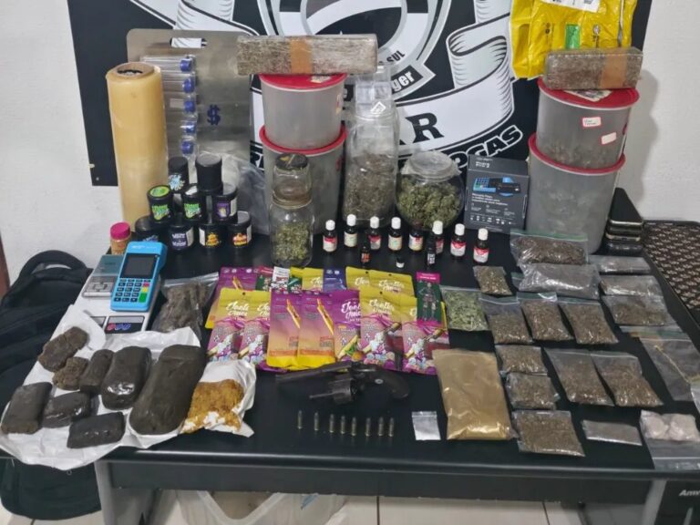 Evidências apreendidas em operação policial: drogas, balanças, equipamentos e arma sobre mesa