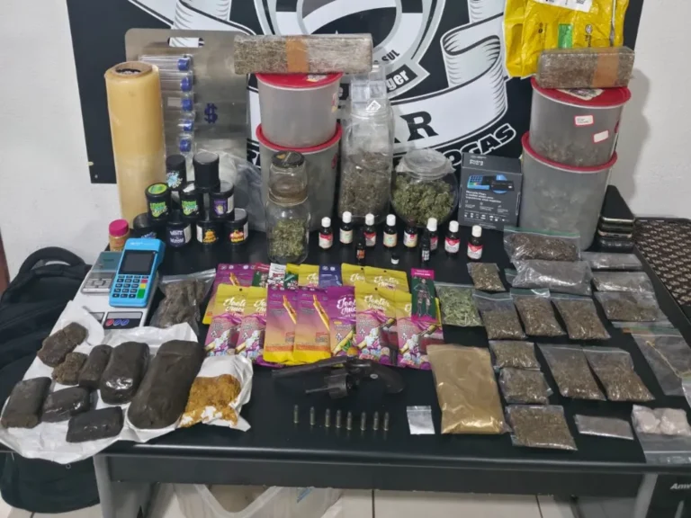 Evidências apreendidas em operação policial: drogas, balanças, equipamentos e arma sobre mesa