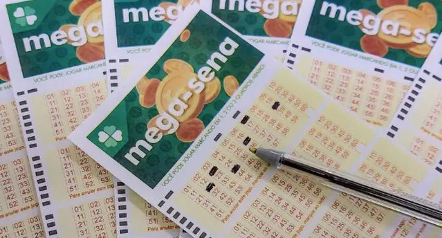 Bilhete da Mega-Sena e lápis sobre mesa, com sorteio ao fundo