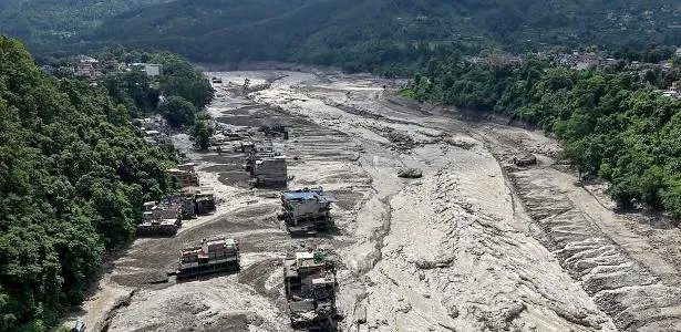 Vista aérea da devastação causada pela avalanche de lama no Nepal, com ponte destruída e casas inundadas