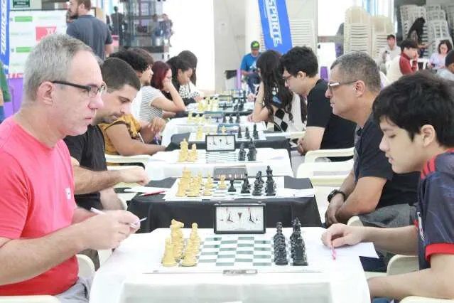 Jogadores de xadrez em um torneio, com tabuleiros e troféu ao fundo