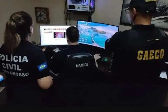 Tornozeleira eletrônica sobre uma mesa com laptop ao fundo