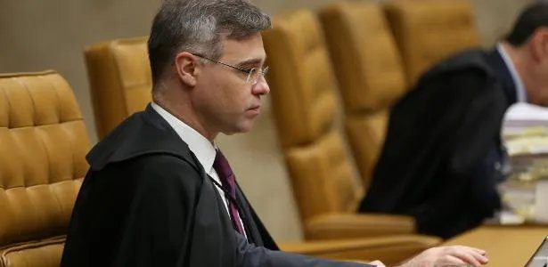Ministro do STF André Mendonça em seu gabinete, com documentos sigilosos sobre a mesa e uma lupa, representando a investigação de vazamento.
