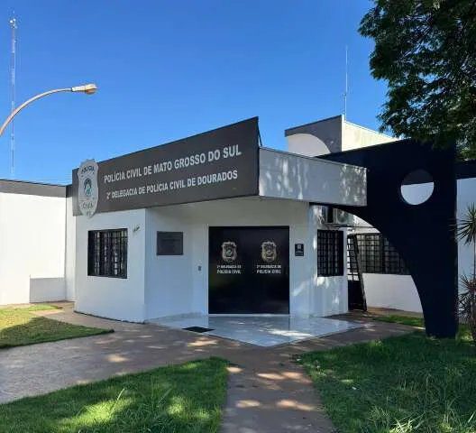 Viatura da Polícia Civil e idoso algemado em frente a uma casa em Dourados.