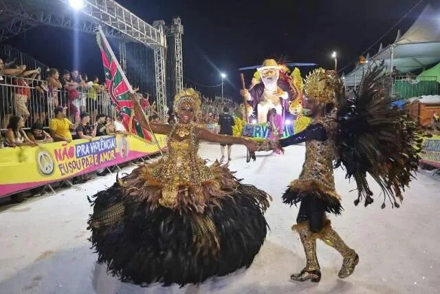Carro alegórico e passistas em desfile de Carnaval à noite em Campo Grande