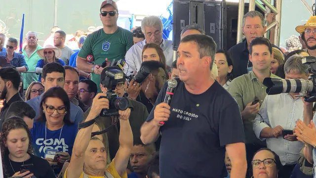 Governador Eduardo Riedel discursando em convenção partidária com bandeiras ao fundo