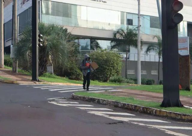 Ruas alagadas e pessoas enfrentando o frio em Campo Grande após forte chuva.